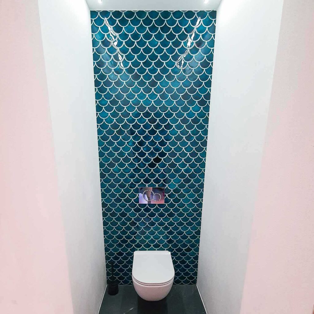 Ceramic mosaic tiles - fish scales, petrol blue color, wall behind the toilet.